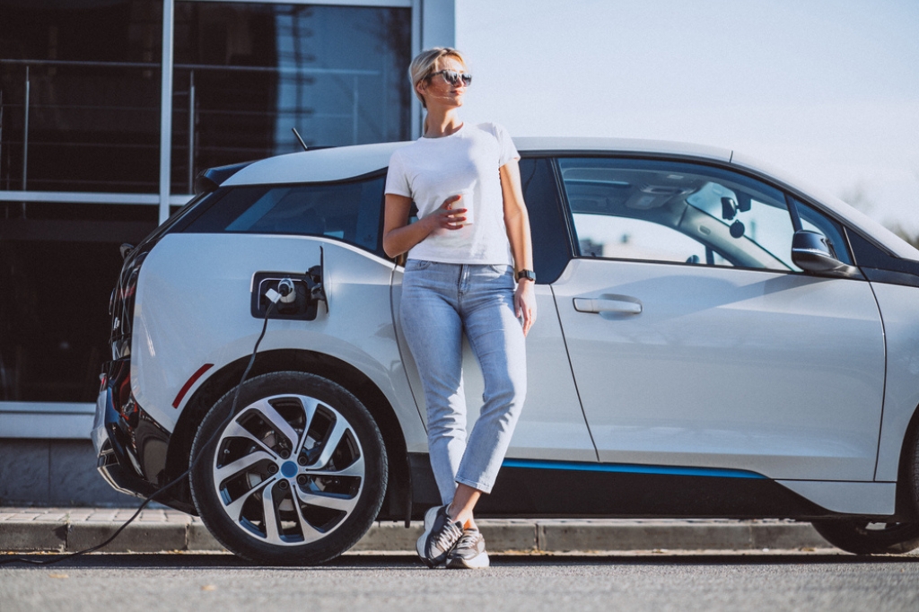 A woman standing beside her used EV leased car.