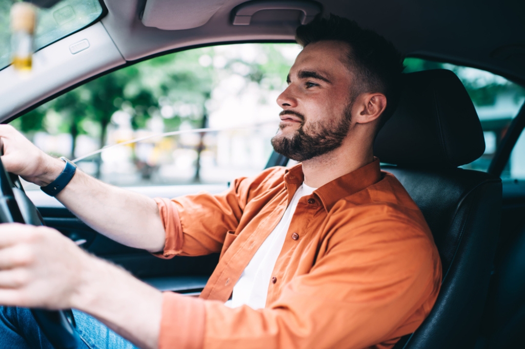 A man in an orange shirt drives a car